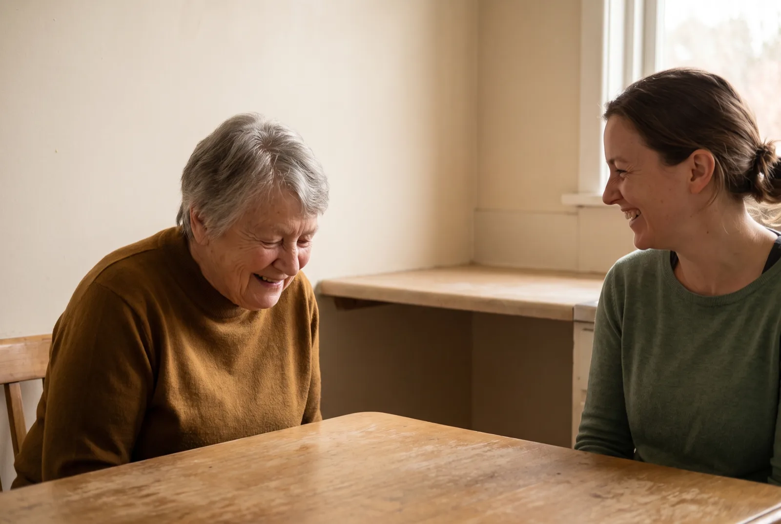 A grandmother and her adult granddaughter laughing together across a kitchen table